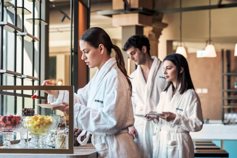 Tre persone in accappatoio si godono una pausa pranzo salutare e benessere con frutta fresca.
