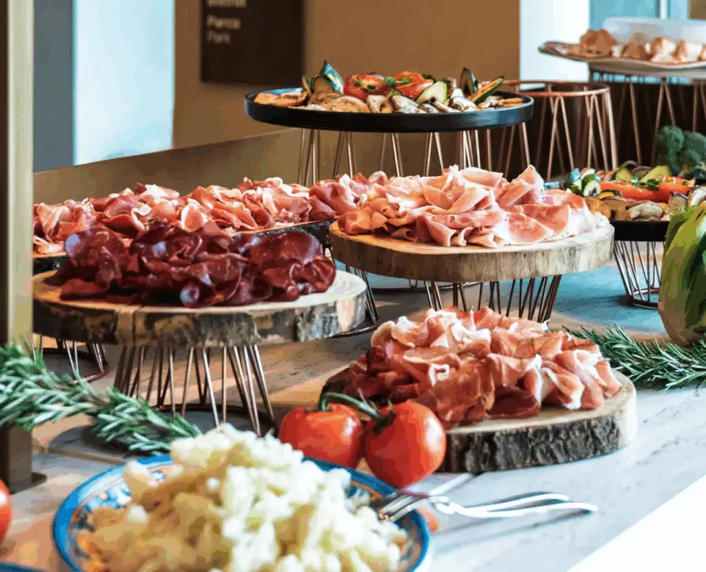 Large selection of cold meats and vegetables served on wooden buffet trays.