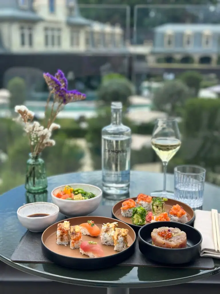 Elegant outdoor dinner with sushi, a bottle of water and a glass of white wine.