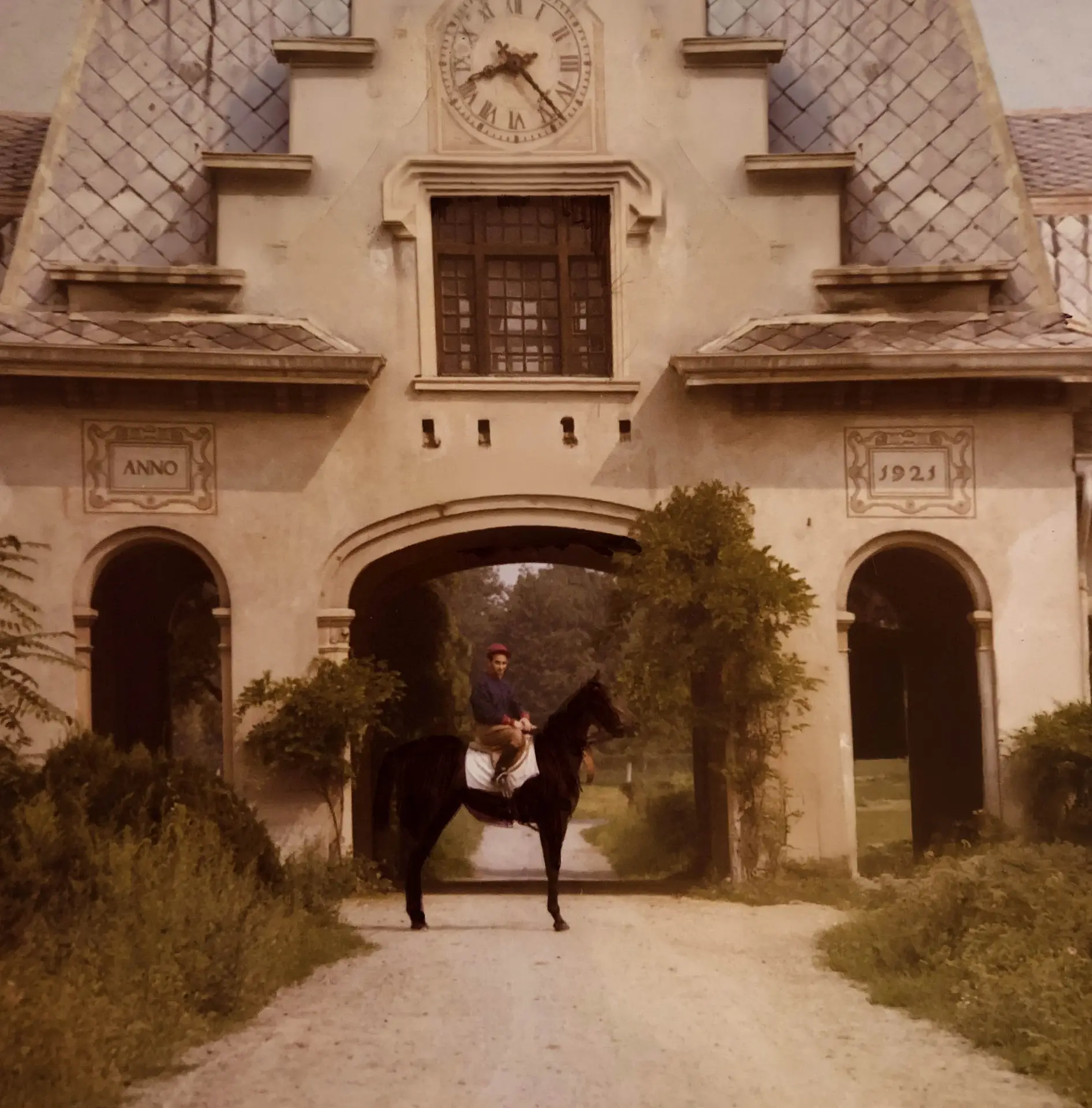 Persona in tenuta da cavallerizza a cavallo, che passa attraverso un arco di pietra con la scritta "1921".