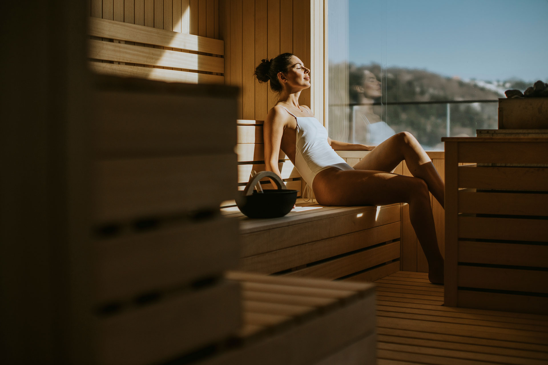 Donna che si rilassa in una sauna in legno sostenibile, godendosi la luce del sole.