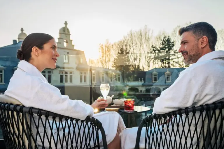 Una coppia in vestaglia si gode un drink su un balcone al tramonto.